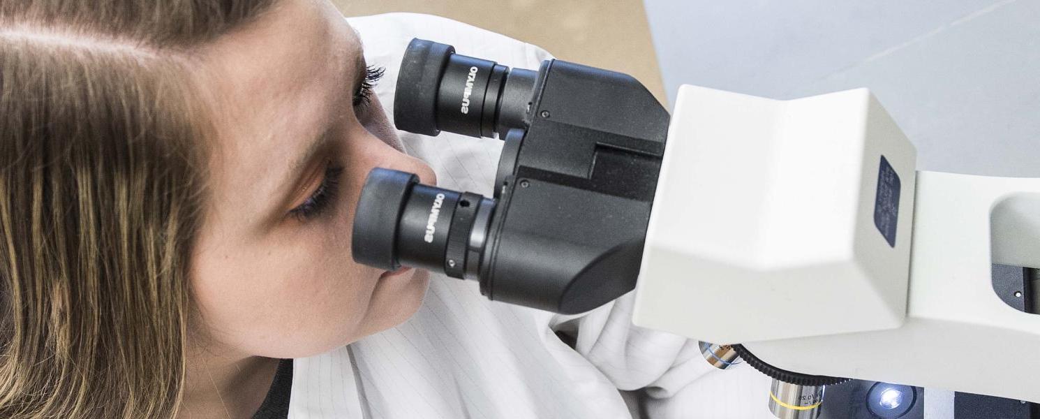 Biology student examining a slide sample on a lab microscope.